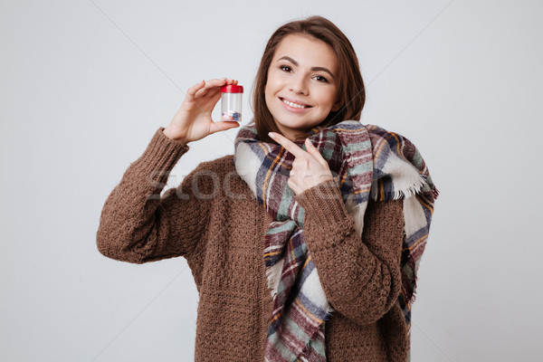 Sick young lady in sweater and scarf holding medicine pills. Stock photo © deandrobot