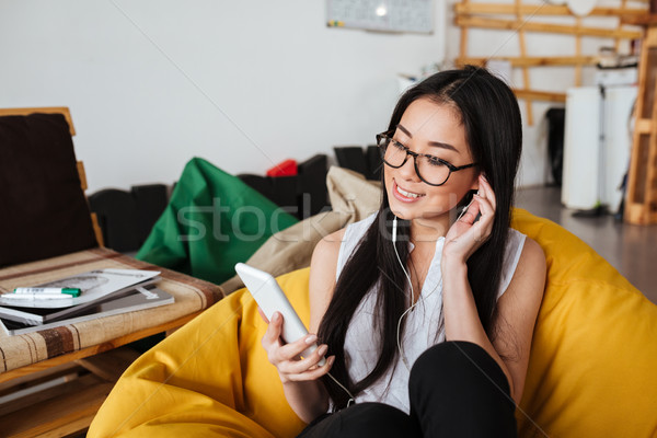 Smiling woman sitting and listening to music from cell phone Stock photo © deandrobot