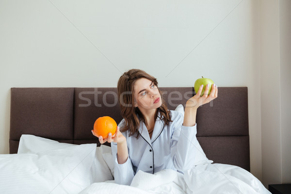 Concentrated young lady choosing between orange and apple Stock photo © deandrobot