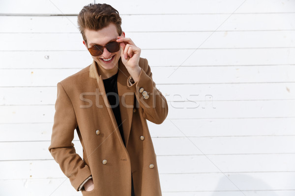 Glücklich junger Mann Mantel stehen schauen Sonnenbrillen Stock foto © deandrobot