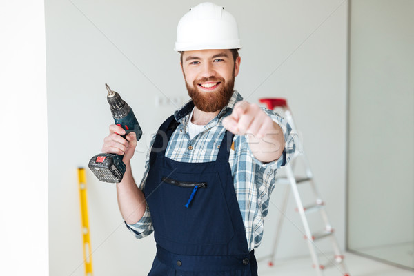 Young man with drill pointing at camera Stock photo © deandrobot