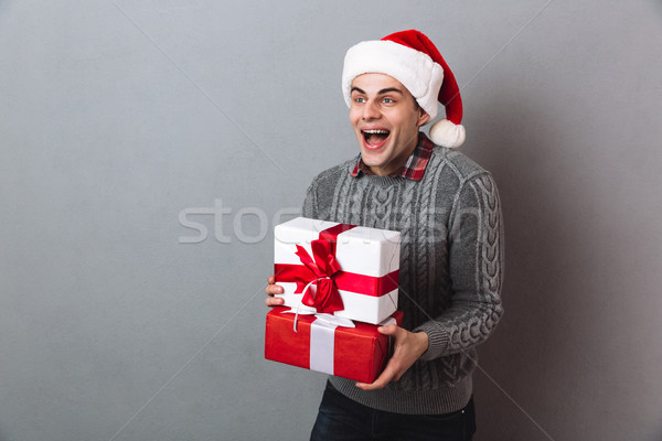 Cheerful man in sweater and christmas hat holding gifts Stock photo © deandrobot