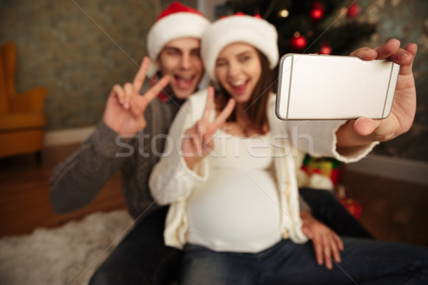 Smiling cheery pregnant woman with her husband celebrating christmas while sitting together on a flo Stock photo © deandrobot