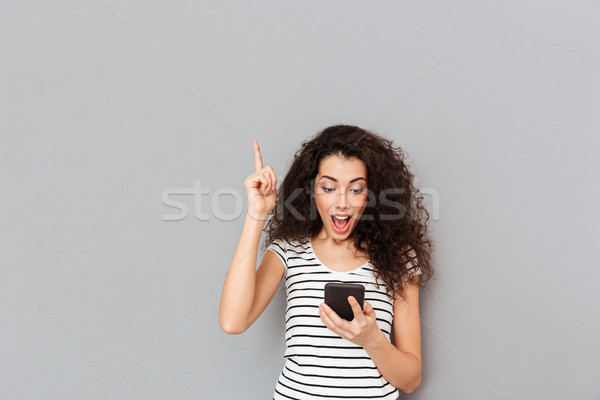 Curious woman looking at mobile phone keeping index finger point Stock photo © deandrobot