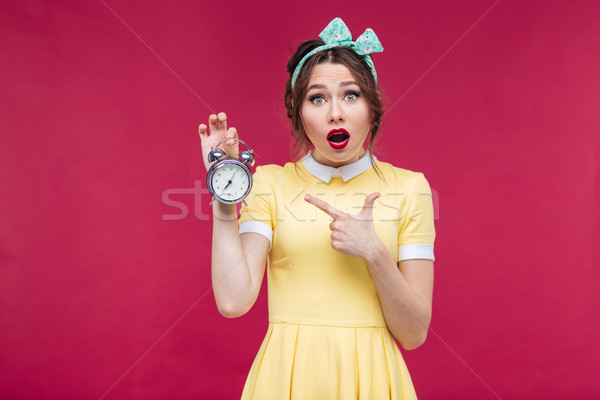Cute amazed pinup girl pointing on alarm clock Stock photo © deandrobot