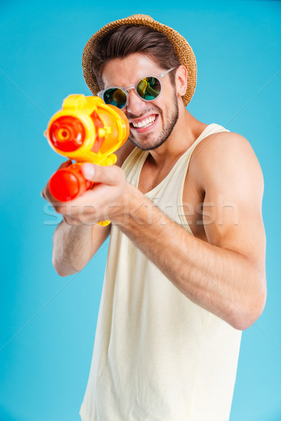 Cheerful young man having fun using water gun Stock photo © deandrobot