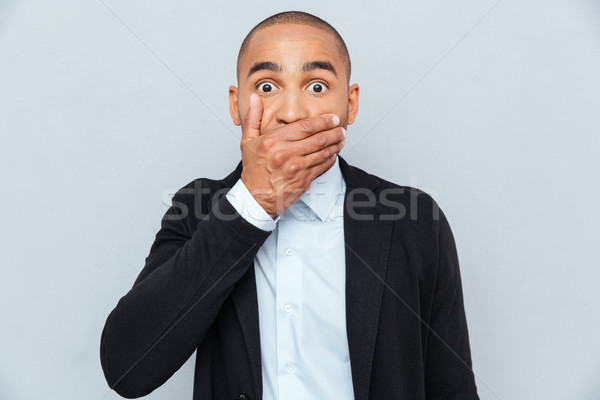 Handsome african man covering mouth with hand isolated on gray Stock photo © deandrobot