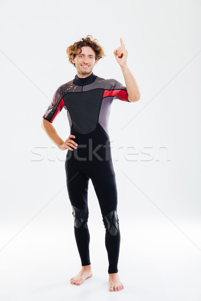 Smiling happy sportsman in diving suit pointing finger up Stock photo © deandrobot