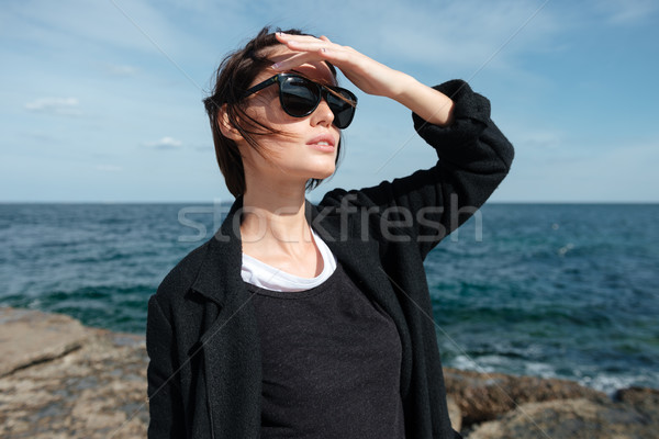 Woman in sunglasses standing and looking far away on seashore Stock photo © deandrobot