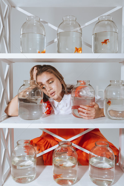 Sad tired young woman leaning on shelf with gold fishes Stock photo © deandrobot