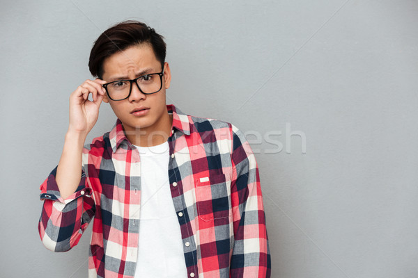 Confused young asian man over grey background Stock photo © deandrobot