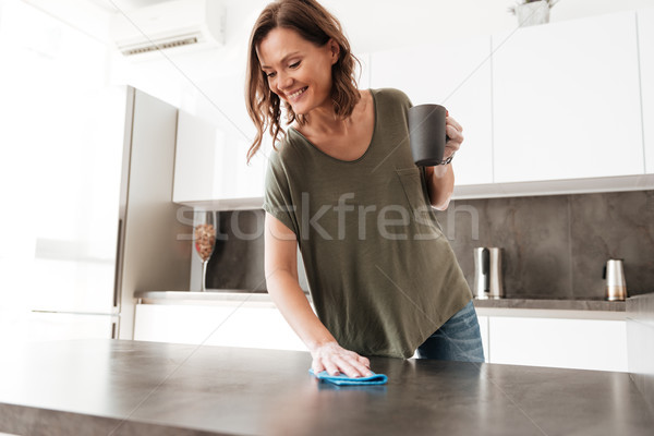 Smiling casual woman wipes a table on kitchen Stock photo © deandrobot