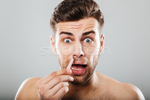 Scared man removing nose hair with tweezers Stock photo © deandrobot