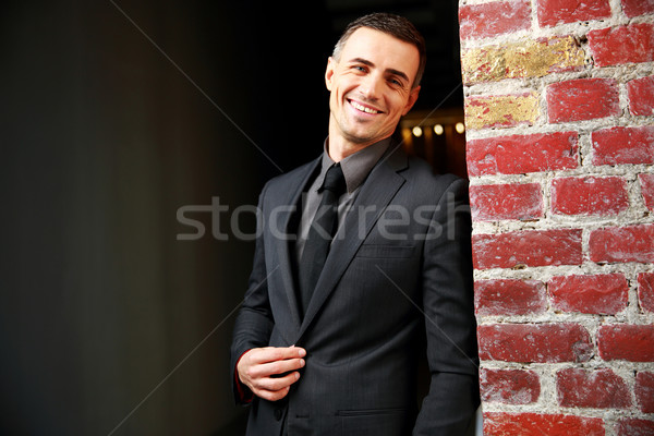 Portrait of a smiling businessman standing near brick wall Stock photo © deandrobot