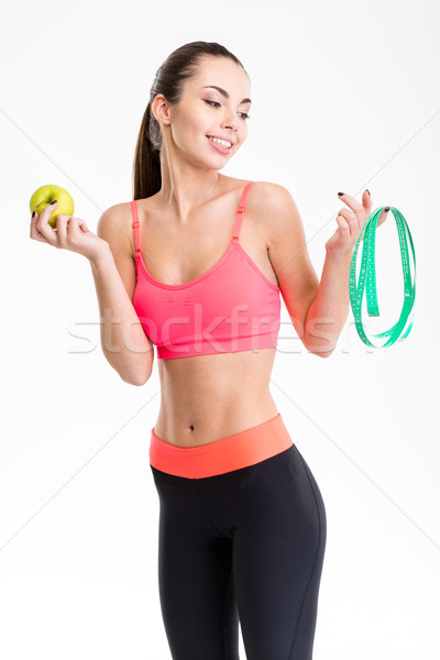 Beautiful happy young sportswoman holding measuring tape and an apple Stock photo © deandrobot