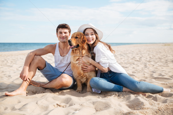 Young smiling couple in love sitting on beach with dog Stock photo © deandrobot