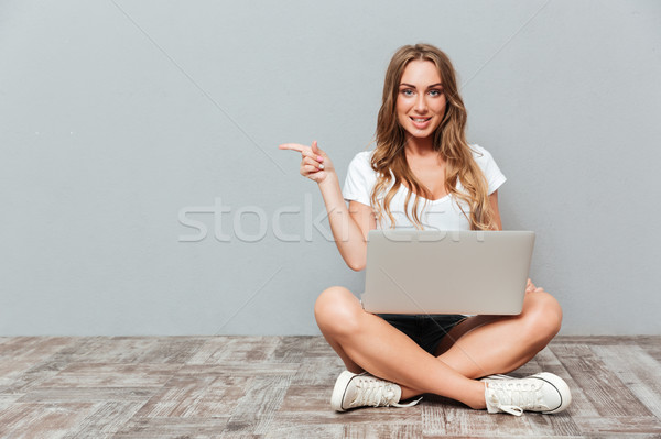 Kobieta posiedzenia piętrze laptop wskazując palec Zdjęcia stock © deandrobot