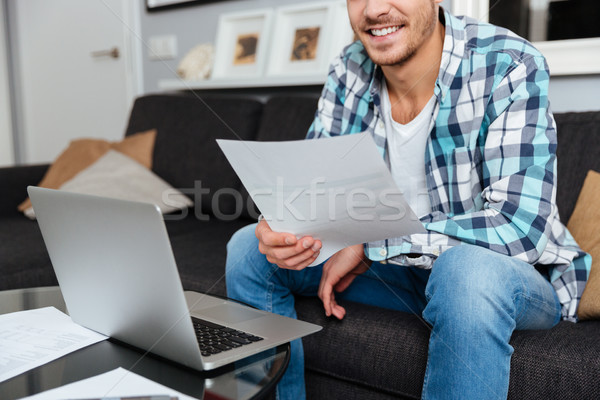Cropped photo of young man using laptop while holding documents Stock photo © deandrobot