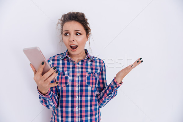Meglepődött nő kockás póló tart telefon Stock fotó © deandrobot