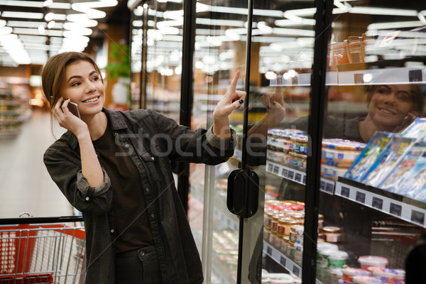 Cheerful young lady standing in supermarket choosing products Stock photo © deandrobot
