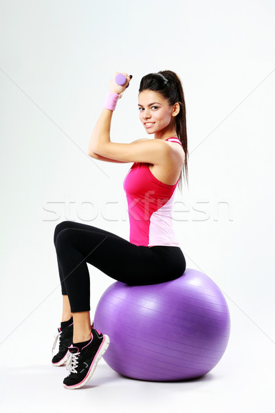 Side view of a young happy sport woman sitting on fitball with dumbells on gray background Stock photo © deandrobot