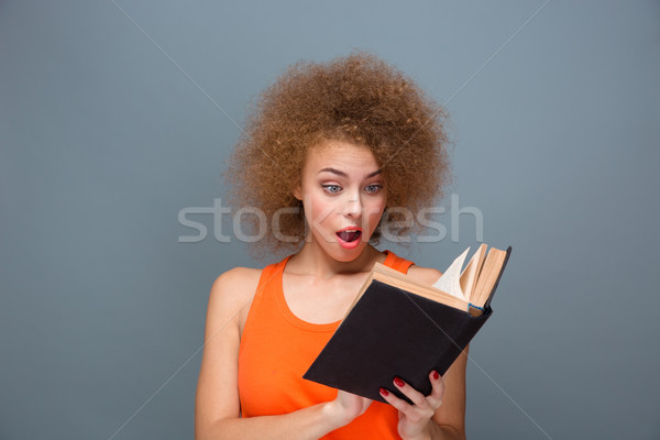 Wondered curly young female reading book Stock photo © deandrobot