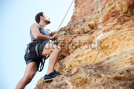 Young sportsman climbing up a rock cliff Stock photo © deandrobot