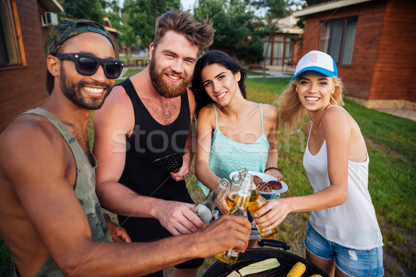 Group of happy friends drinking beer and having barbecue outdoors Stock photo © deandrobot