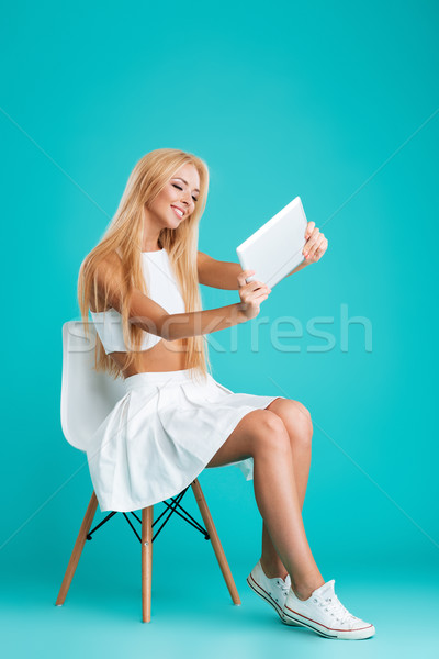 Woman sitting on chair and playing games with tablet computer Stock photo © deandrobot