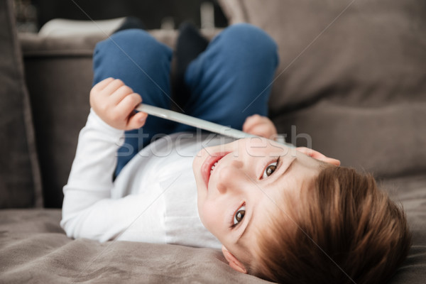 Happy little boy holding tablet computer while lies on sofa Stock photo © deandrobot