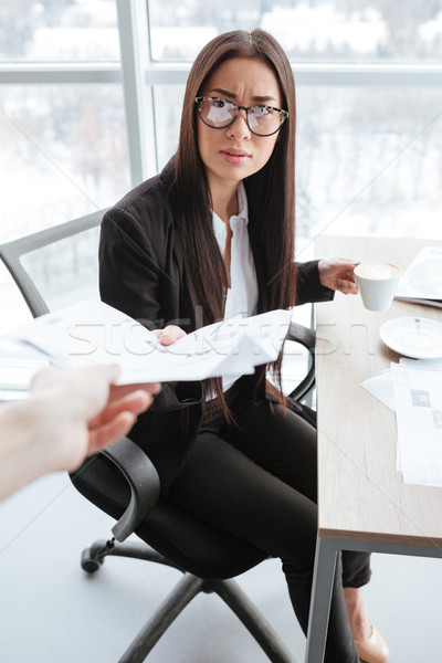 Stock photo: Serious businesswoman receiving documents and drinking coffee at the table