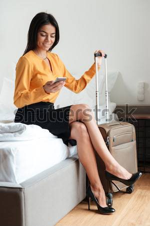Kobieta posiedzenia hotel bed walizkę skrzyżowanymi nogami Zdjęcia stock © deandrobot