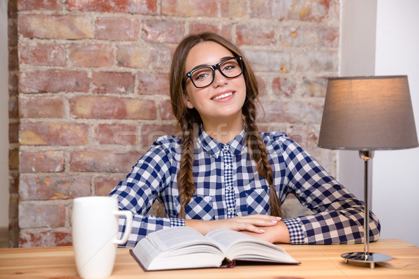 Happy woman in glasses sitting at the table with book Stock photo © deandrobot