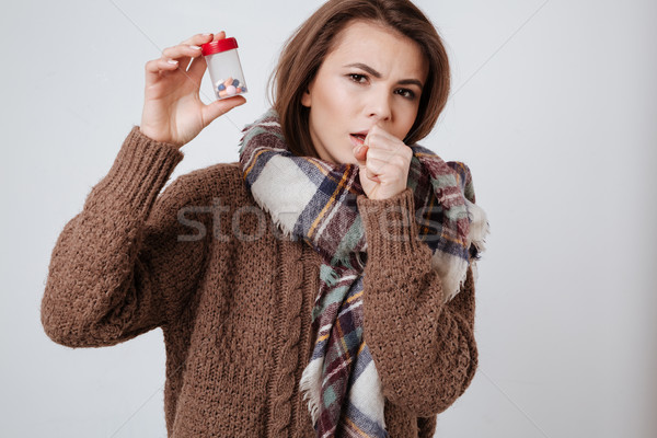 Sick young woman in sweater and scarf holding medicine pills. Stock photo © deandrobot