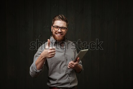 Man in eyeglasses holding tablet computer and pointing finger away Stock photo © deandrobot
