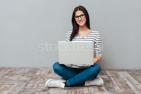 Young cheerful woman sitting on floor while using laptop Stock photo © deandrobot