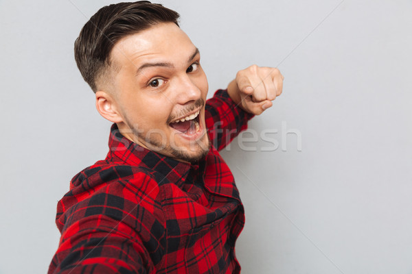Smiling man standing sideways and pointing at camera Stock photo © deandrobot