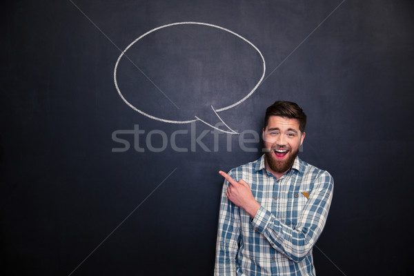 Cheerful man pointing away over blackboard background with  speech bubble Stock photo © deandrobot