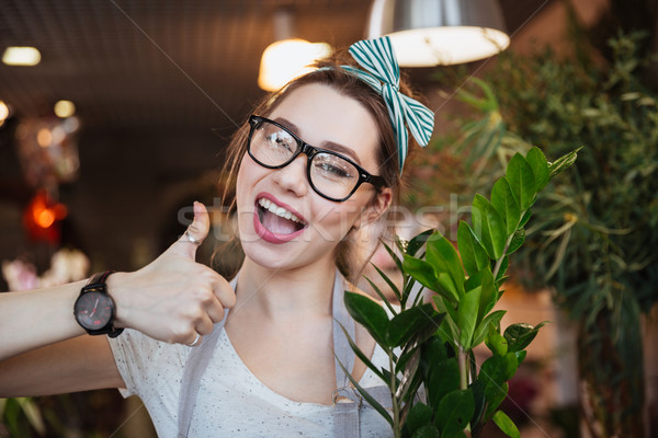 Happy woman florist showing thumbs up in flower shop Stock photo © deandrobot