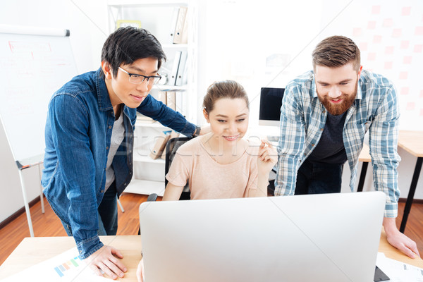 Smiling woman and two men working with computer in office Stock photo © deandrobot