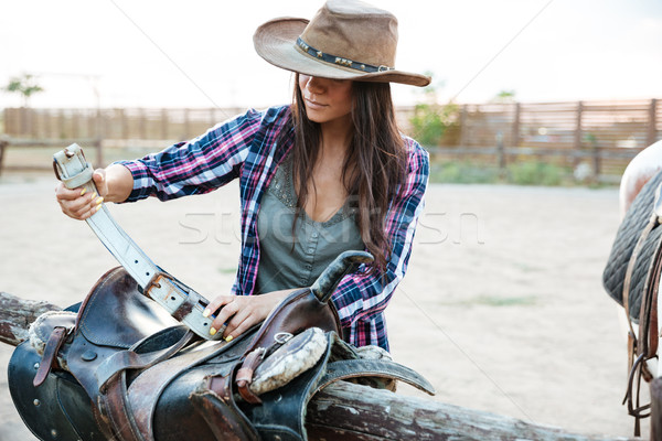 Woman cowgirl standing and preparing saddle for riding horse Stock photo © deandrobot