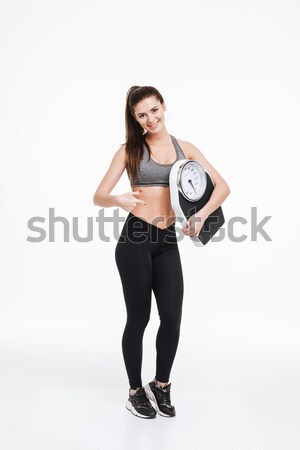 Smiling pretty sports woman standing and pointing finger at scales Stock photo © deandrobot