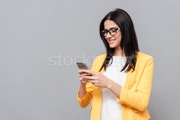 Cheerful woman chatting by her phone over grey background Stock photo © deandrobot
