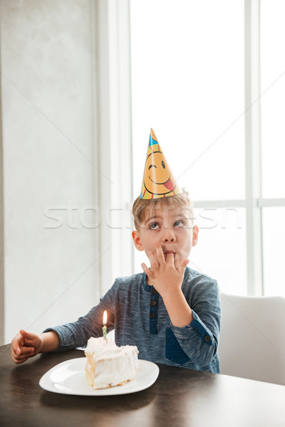 Birthday boy sitting in kitchen near cake and eating Stock photo © deandrobot