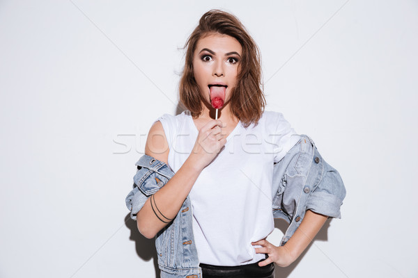Funny lady dressed in jeans jacket eating candy. Stock photo © deandrobot