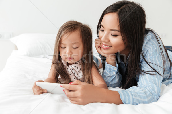 Mosolygó nő kicsi lánygyermek néz mobiltelefon mosolyog Stock fotó © deandrobot