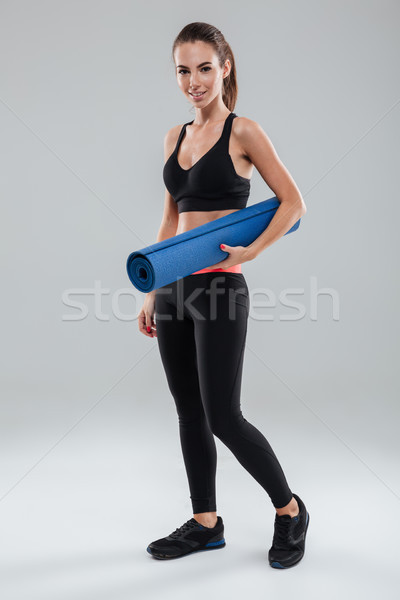 Full length image of smiling fitness woman holding fitness mat Stock photo © deandrobot