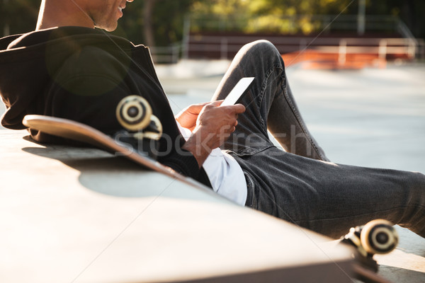 Cropped image of a smiling skateboarder looking at mobile phone Stock photo © deandrobot