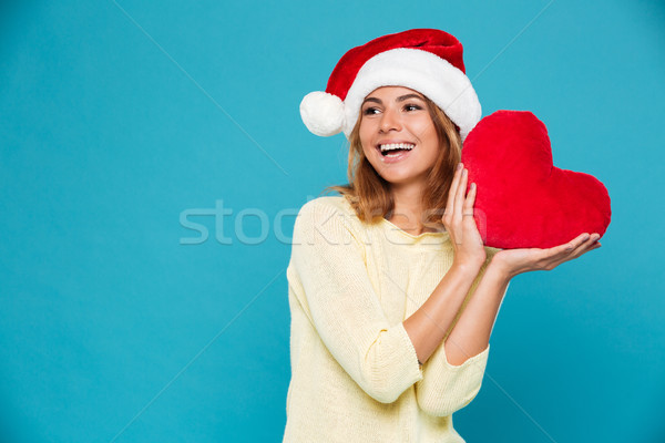 Close-up photo of happy girl in yellow blouse and Santa's hat holding red soft heart, looking aside Stock photo © deandrobot