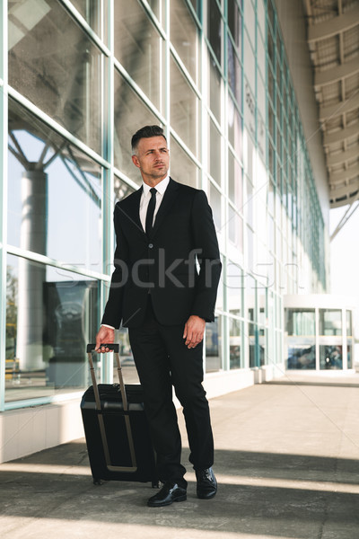 Bájos üzletember öltöny sétál bőrönd kívül Stock fotó © deandrobot